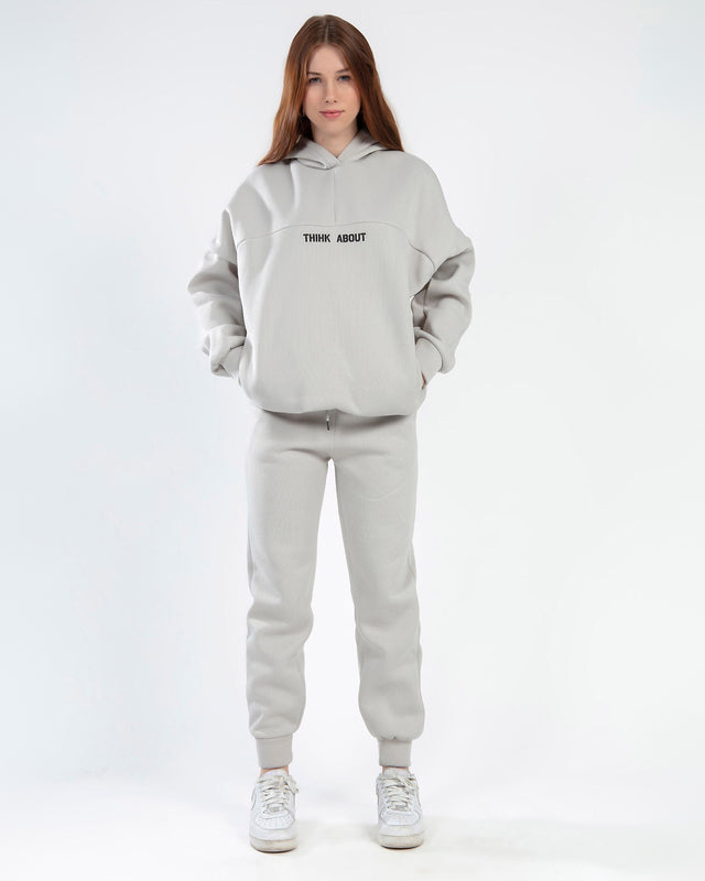 Model wearing the Freya light grey two-piece athleisure set with an oversized 'THINK ABOUT' hoodie and matching joggers.