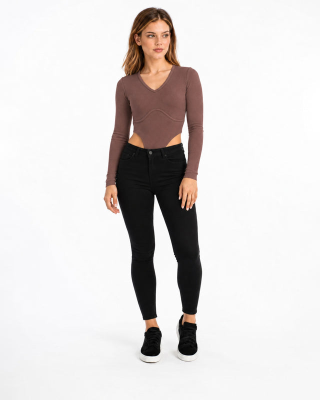 A model poses in a fitted long-sleeve top with a V-neck and cut-out details, paired with black skinny jeans and sneak...