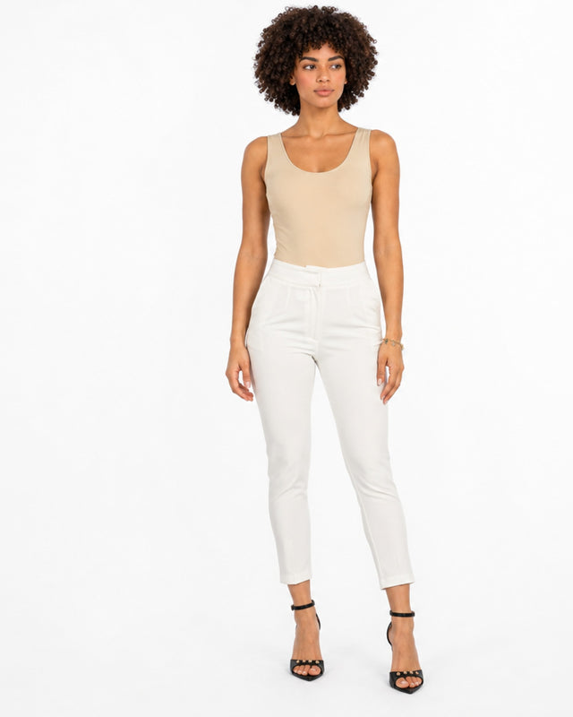 A model wearing a fitted beige bodysuit paired with tailored white pants and black strappy heels.