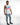 A man poses in a sleeveless white top with colorful text, paired with distressed light blue jeans and casual sneakers.