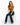 A woman sits on a white cube, wearing a rust-colored cropped top and flared dark jeans, with black heels.