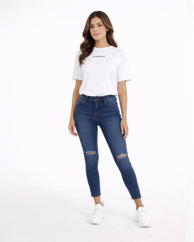 A woman stands confidently in a casual white t-shirt and fitted blue jeans with distressed details.