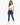 A woman poses in a fitted white crop top and blue skinny jeans, paired with white sneakers.