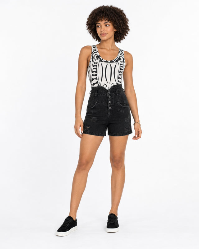 A model with curly hair wears a patterned tank top and high-waisted black shorts, paired with black sneakers.
