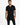A man stands confidently in a fitted black overall with a short-sleeve design and a belted waist.
