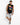 A man stands casually in a sleeveless black shirt with colorful graphic text, paired with distressed gray shorts and...