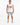 A man stands confidently in a sleeveless white shirt with colorful graphic text, paired with distressed gray shorts a...