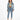 A woman stands confidently in a cropped denim jacket, fitted top, and high-waisted jeans, paired with white sneakers.