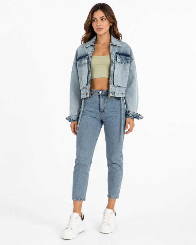 A woman stands confidently in a cropped denim jacket, fitted top, and high-waisted jeans, paired with white sneakers.