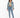 A woman stands confidently in a light denim jacket, green crop top, and fitted blue jeans, paired with white sneakers.
