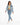 A woman walks confidently in a cropped denim jacket, fitted green top, and light blue jeans paired with white sneakers.