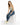 A woman sits on a white cube, wearing a light green tank top, distressed blue jeans, and white sneakers with neon acc...