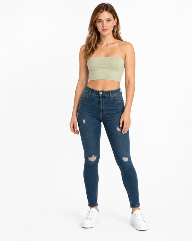 A model wearing a light green cropped top with spaghetti straps paired with distressed blue jeans and white sneakers.