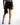 Harlow black satin mini skirt with fringe hem and wrap detail on model, paired with high heels.