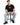 A man sits on a black stool wearing a black t-shirt and light blue jeans, paired with black sneakers.