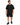A man stands wearing a loose-fitting black t-shirt and matching shorts, paired with black sneakers.