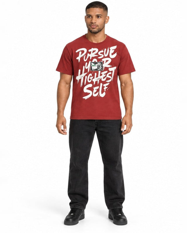 A man stands wearing a red graphic t-shirt with bold white text and black jeans, showcasing a casual style.