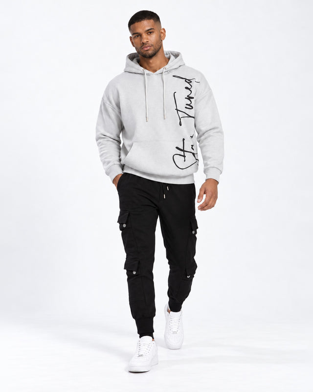 A man walks confidently in a light gray hoodie and black cargo pants, paired with white sneakers.