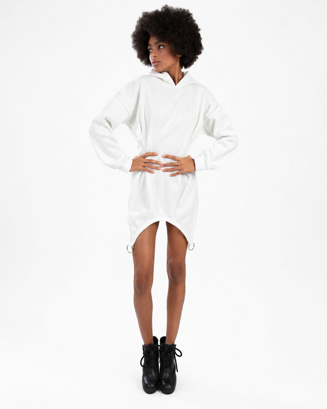 A model poses in a white hooded dress with side rings, paired with black ankle boots against a plain background.
