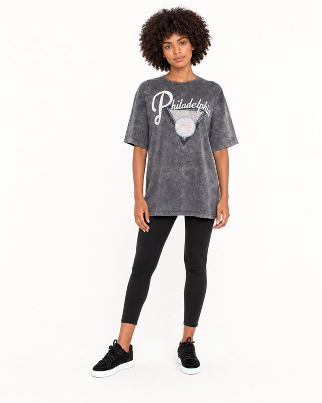 A model wearing a loose-fitting, gray graphic tee with "Philadelphia" text, paired with black leggings and sneakers.