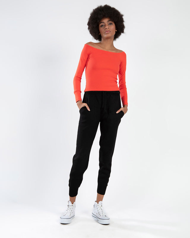 Model in a red off-the-shoulder long sleeve top paired with black joggers and white high-top sneakers.