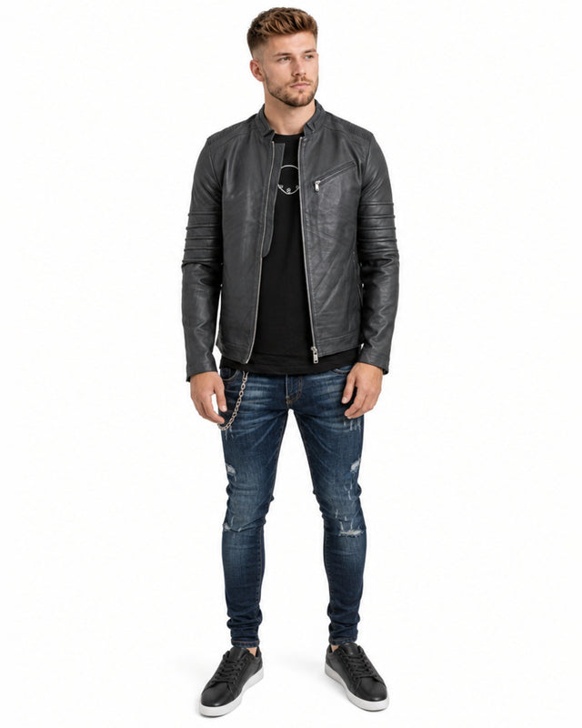 A man stands confidently in a fitted gray jacket, paired with a black t-shirt and distressed jeans.