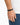A close-up of a hand wearing a black beaded bracelet with a sleek clasp, set against a light background.
