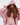 A young woman with long, wavy hair wears a pink oversized hoodie and matching outfit, showcasing a stylish cutout des...