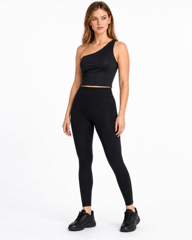 A model poses in a sleek black one-shoulder activewear top paired with matching leggings and sneakers.