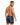A man with short hair poses from the back, wearing black swim shorts featuring a floral pattern.