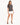A woman stands confidently in a gray t-shirt paired with a white mini skirt and black high-heeled sandals.