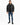 A man stands wearing a black puffer coat, black shirt, distressed jeans, and sneakers against a white background.