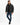 A man wearing a black puffer coat, black shirt, distressed jeans, and sneakers poses against a white background.