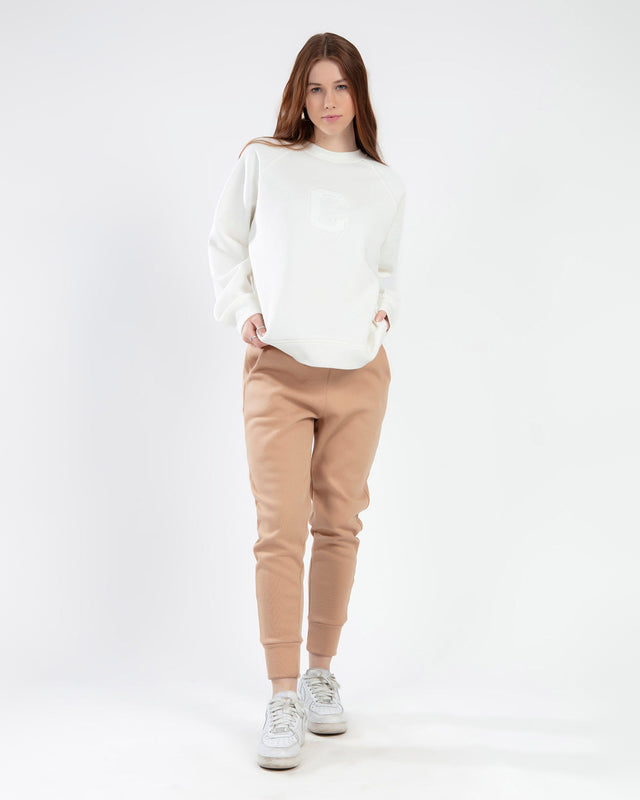 Model in cream crewneck sweatshirt with 'C' logo and tan jogger sweatpants. Gen Z streetwear loungewear set.