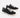 Black canvas sneakers with white laces and rubber soles, featuring a casual design and contrasting stitching.