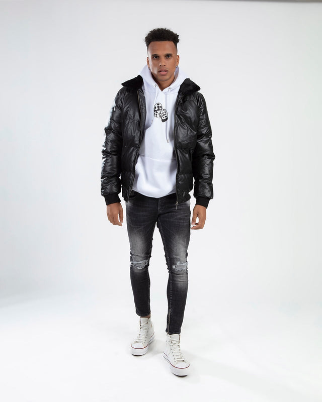 Man in Jerry Puffer Coat, a black insulated jacket with fluffy collar, over a white hoodie and distressed jeans.