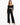 A model poses in black high-waisted pants paired with a cropped off-the-shoulder top and strappy heels.
