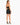 A woman stands in a fitted black crop top and matching skirt, showcasing a sleek silhouette and strappy heels.