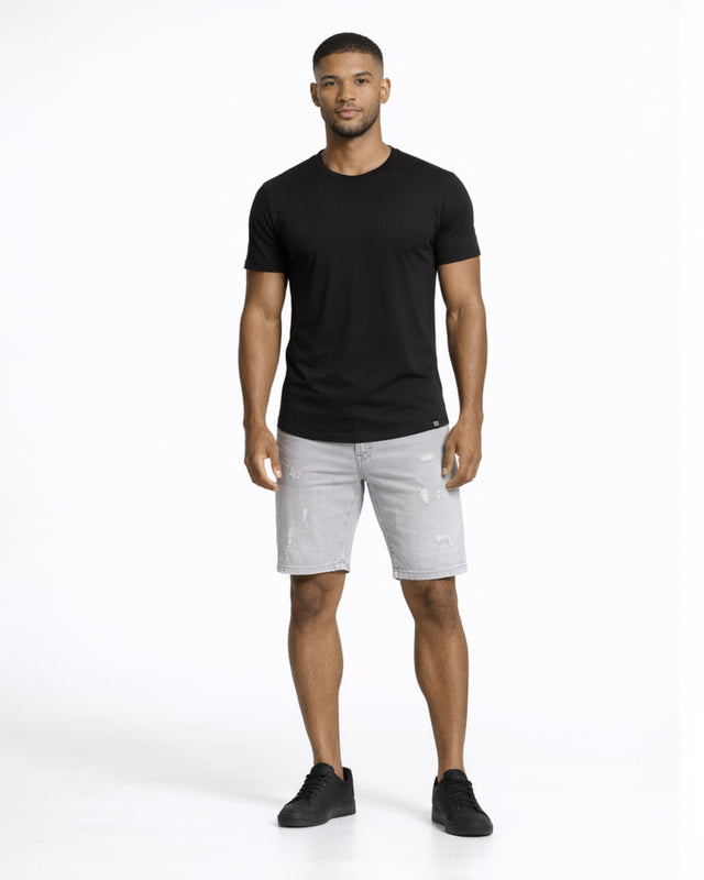 A man stands confidently in a fitted black t-shirt and distressed gray shorts, paired with black sneakers.