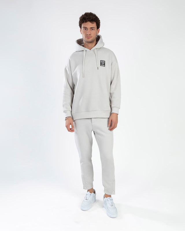 Man in a light grey Rostory oversized hoodie and matching joggers streetwear set with white sneakers.