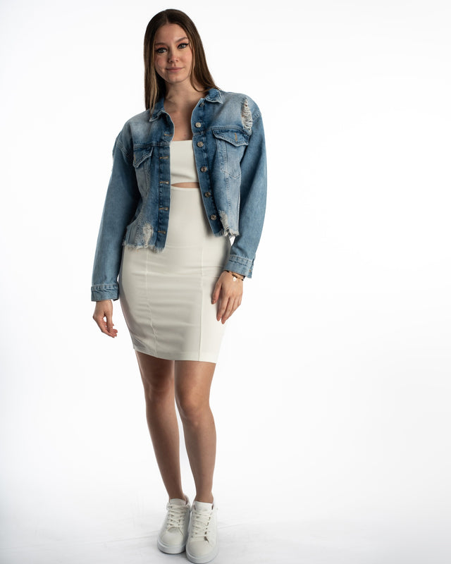 Model in oversized Jolie blue washed denim jacket with distressing, frayed hems, and silver buttons over a white dress.