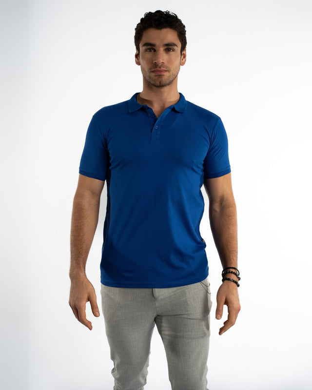 Model wearing a blue Ryan Polo Shirt, a men's casual short sleeve polo paired with grey trousers.