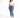 A woman stands confidently in a cropped white top and fitted blue jeans, paired with white sneakers.