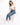 A woman sits on a white cube, wearing a cropped white top and blue skinny jeans, paired with white sneakers.