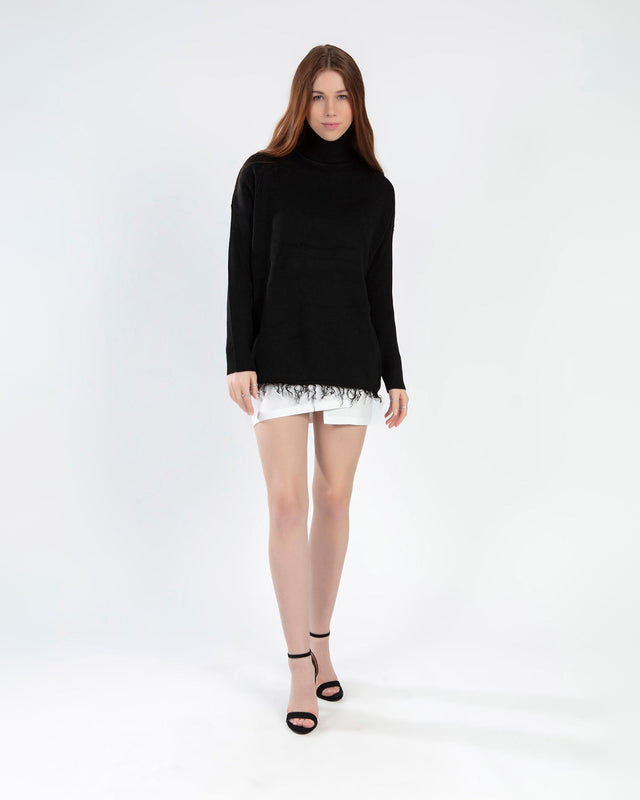 Model wearing a Celine black oversized turtleneck knit sweater with a distressed fringe hem and white mini skirt.