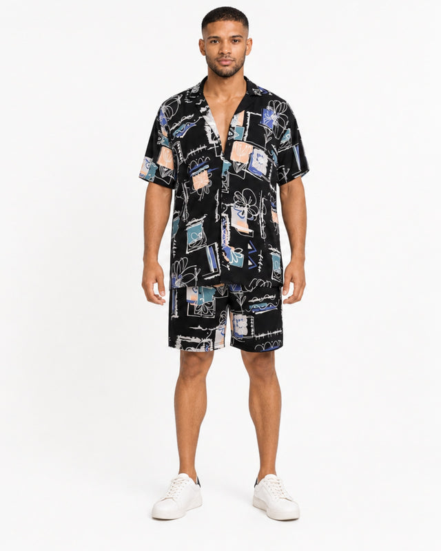 A man stands confidently in a short-sleeve, patterned shirt and matching shorts, paired with white sneakers.