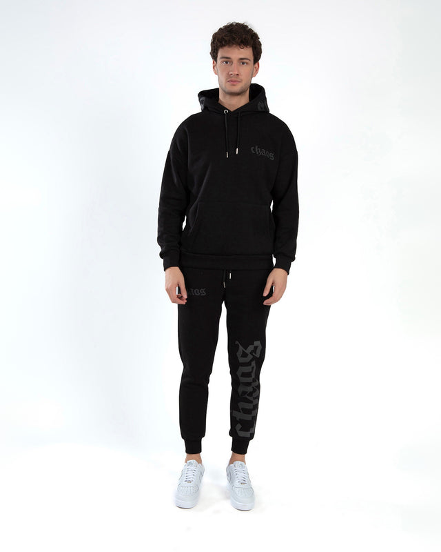 A model wearing a black hoodie and matching sweatpants with graphic text, paired with white sneakers.