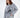 Woman in an oversized light grey streetwear sailing top with a black nautical ship graphic and ribbed cuffs.