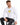 A man sits on a stool wearing a long-sleeve white shirt with a graphic design and dark jeans.