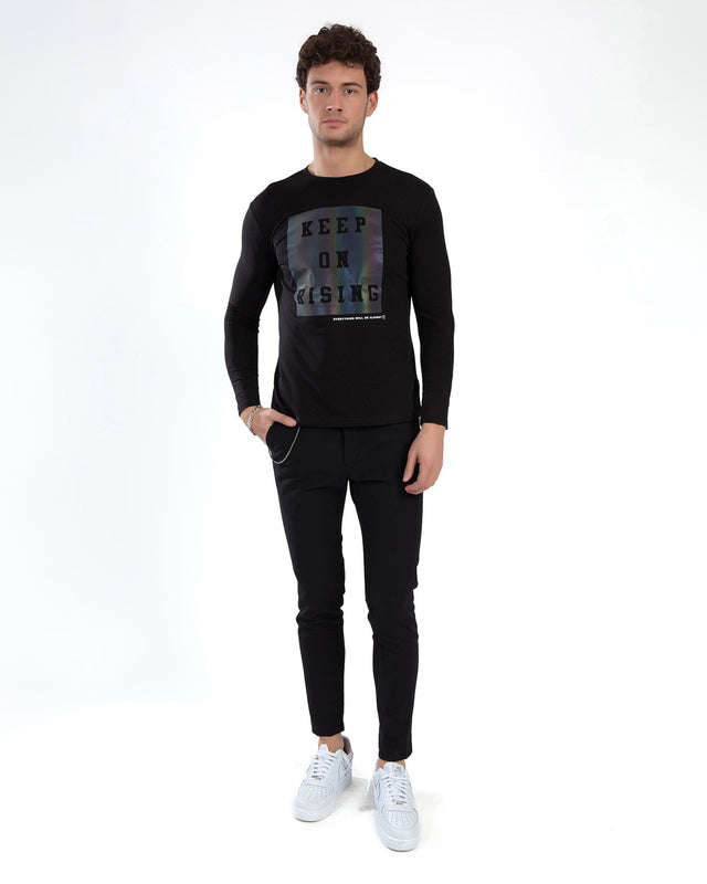 A young man stands confidently in a black long-sleeve shirt with a motivational graphic and black pants.